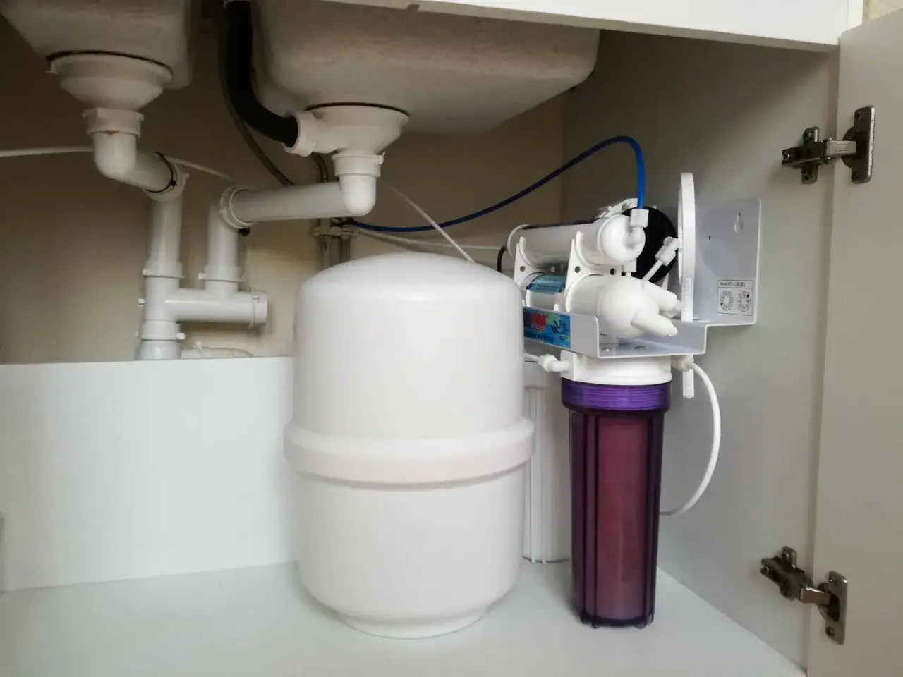 Sous l'&eacute;vier, un syst&egrave;me de filtration d'eau avec r&eacute;servoir blanc et filtre violet. Mon adoucisseur coule en permanence, il faut v&eacute;rifier les tuyaux.