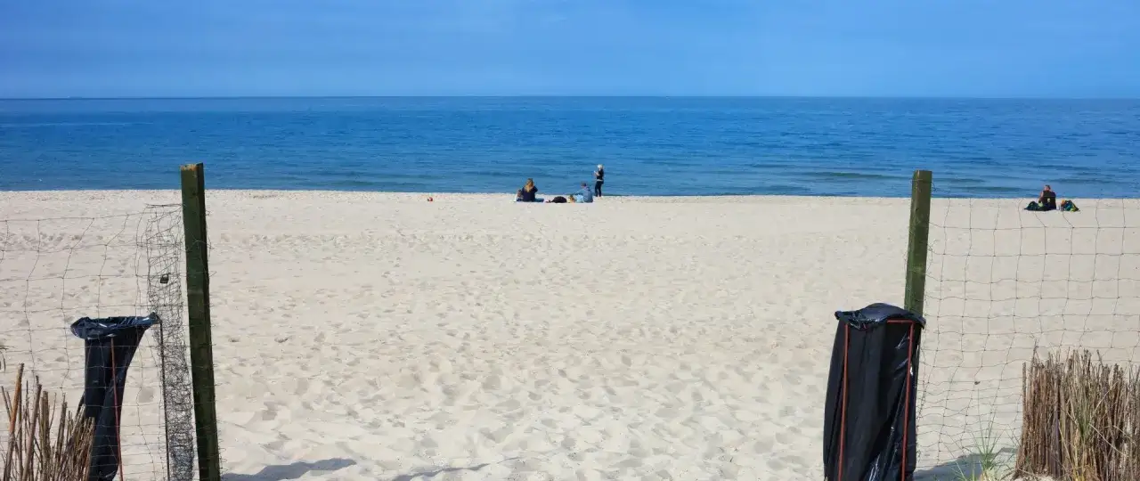 Plaża we Władysławowie, idealne miejsce na wypoczynek. W tle widać morze i kilka osób relaksujących się na piasku. Władysławowo atrakcje dla dzieci to przede wszystkim bezpieczne kąpiele i zabawy na piasku.