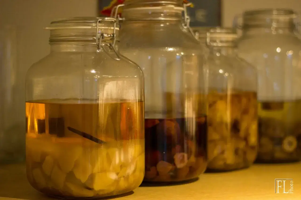 Plusieurs bocaux en verre alignés, dont un rempli de morceaux de mangue et de rhum arrangé.