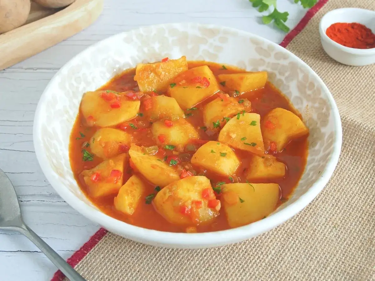 Patatas a la importancia, un plato reconfortante con trozos de patata en una salsa roja especiada, adornado con perejil fresco.