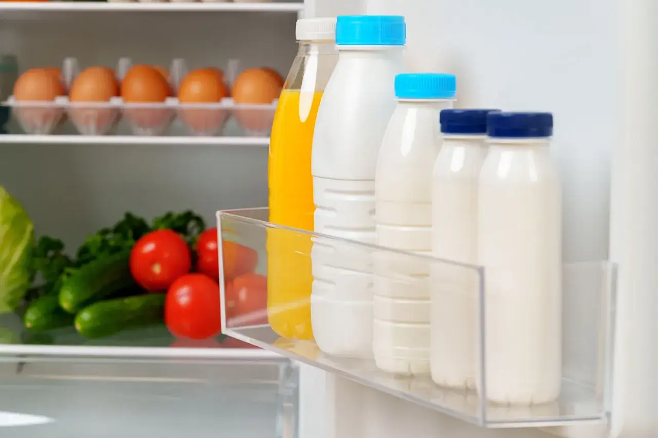 Bouteilles de lait et jus dans un frigo, assurant la conservation des aliments. Des &oelig;ufs et des l&eacute;gumes sont aussi visibles.