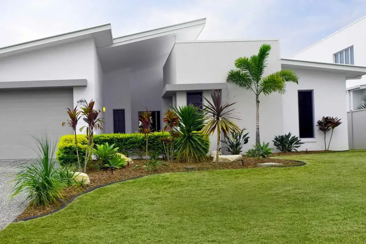 Un beau parterre de fleurs devant une maison moderne aux lignes &eacute;pur&eacute;es. Des plantes tropicales et une pelouse verdoyante compl&egrave;tent le paysage.