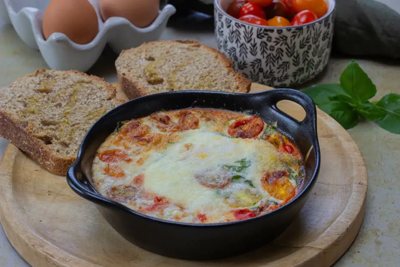 Un plat d'&oelig;ufs au four &agrave; l'italienne, gratin&eacute; et garni de tomates et de basilic, servi avec du pain grill&eacute;.