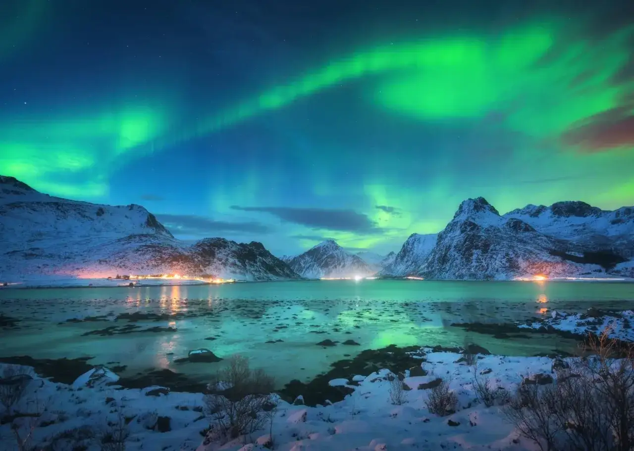 Capturing the Northern Lights: A snowy landscape with a frozen lake reflects the vibrant green aurora borealis dancing across a starry night sky.