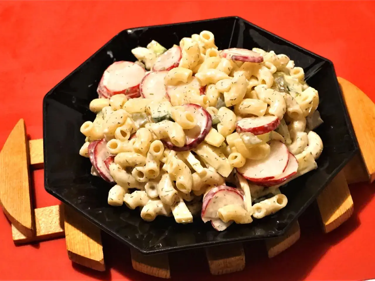 Leckerer Nudelsalat ohne Mayo mit Radieschen und Dill, serviert auf einem schwarzen Teller.