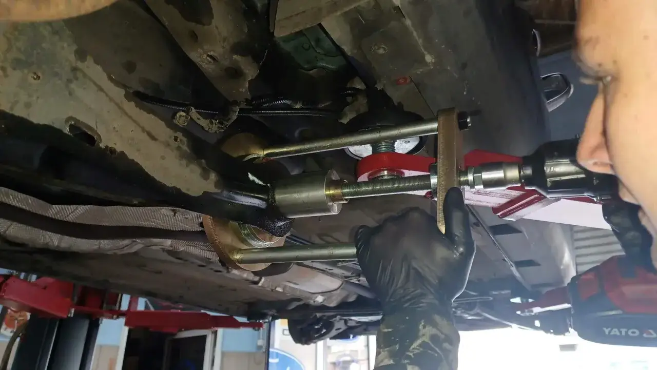 Mechanik w czarnej rękawiczce używa specjalistycznego narzędzia do wymiany tulei wahacza w samochodzie.