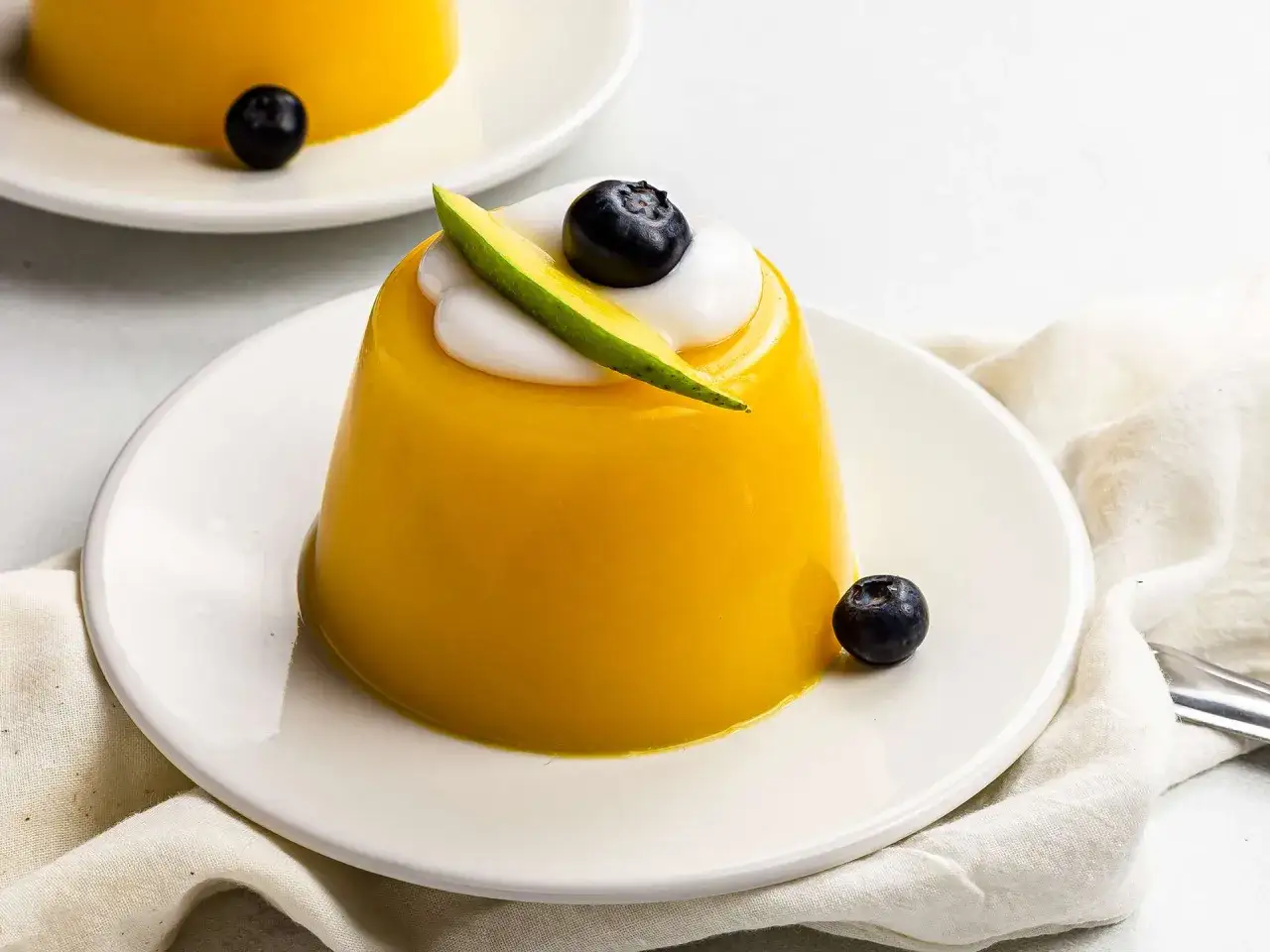 Pyszna, żółta galaretka bez cukru, udekorowana bitą śmietaną, borówką i plasterkiem mango. Zastanawiasz się, ile kalorii ma galaretka bez cukru?
