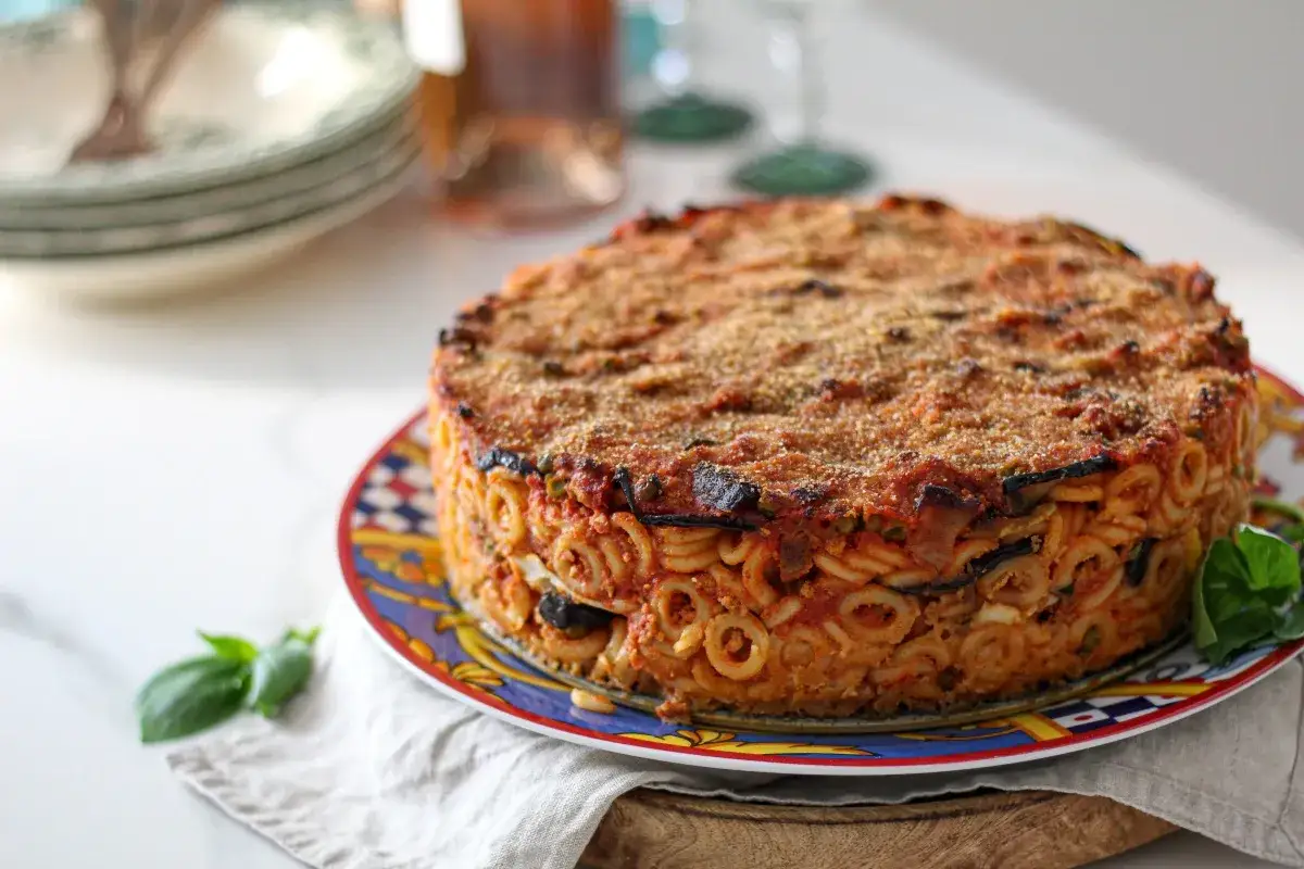 Anelletti alla siciliana, un tortino di pasta al forno con melanzane, sugo e formaggio, pronto per essere gustato.