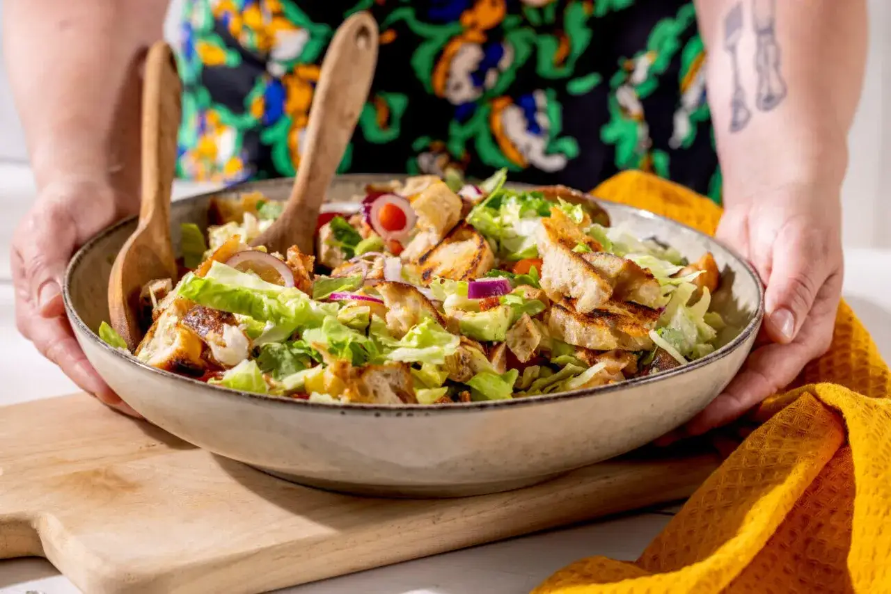 En stor skål med en härlig sallad, perfekt för sommarmat recept. Krispig sallad, rostat bröd och rödlök blandas med träskedar.