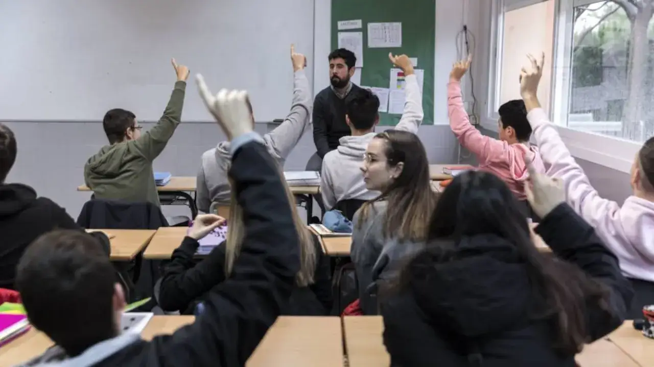 Estudiantes levantan la mano en clase, discutiendo temas de **relaciones internacionales**. El profesor observa atentamente.