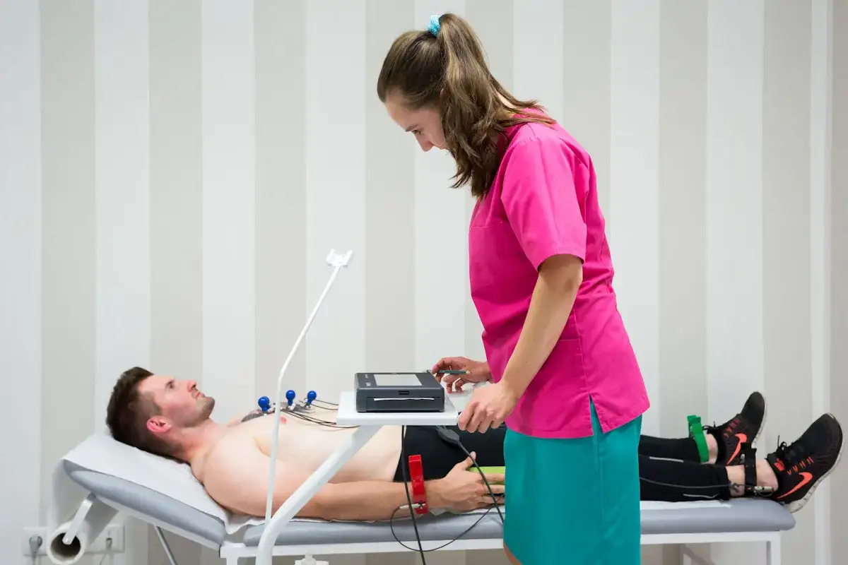 Pacjent leży na kozetce, pielęgniarka przygotowuje aparat EKG. Badanie serca, ile trwa ekg, zależy od jego rodzaju.