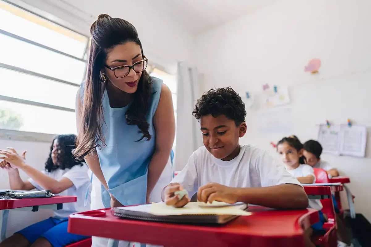 Maestra ayuda a un ni&ntilde;o con s&iacute;ndrome de Down en clase. Ambos sonr&iacute;en mientras trabajan en sus cuadernos.