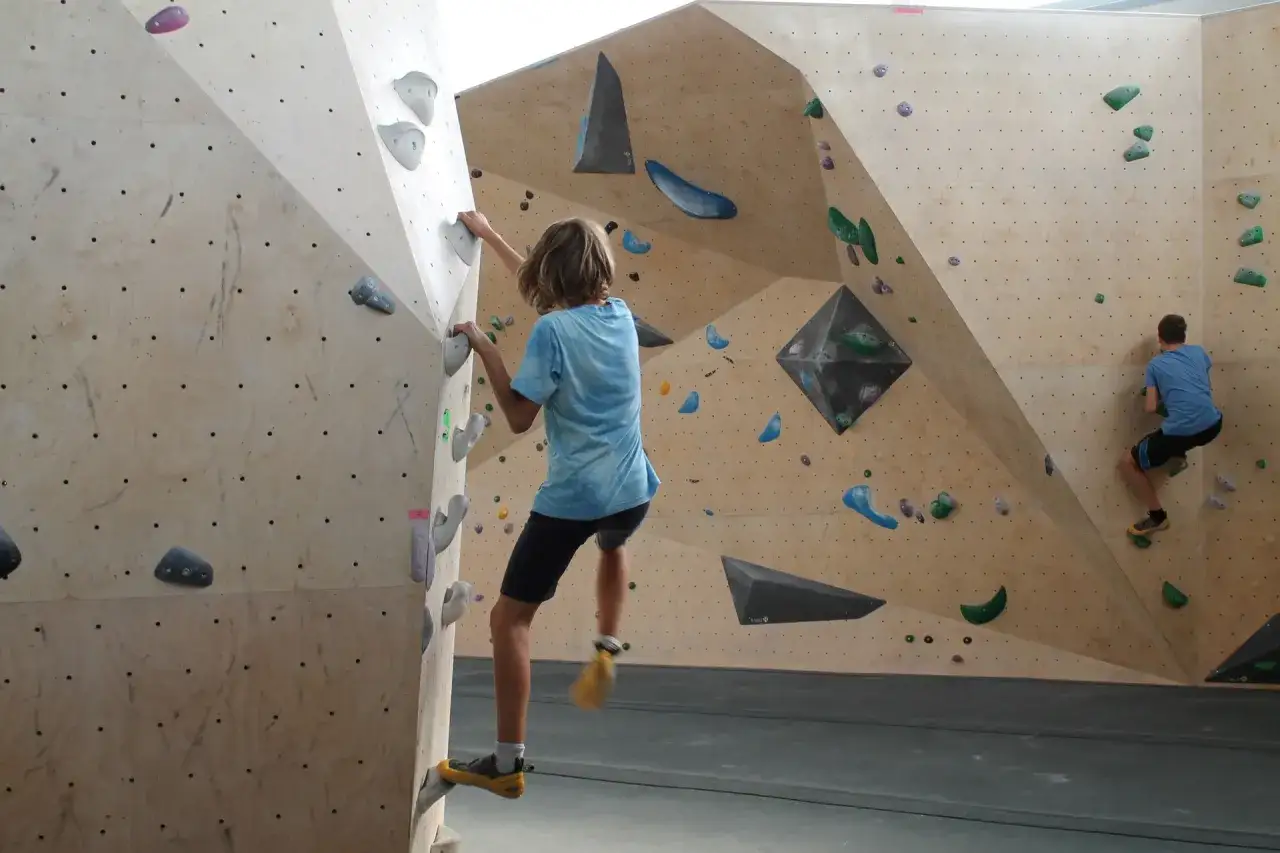 Deux jeunes grimpeurs s'entraînent sur un mur d'escalade, atteignant le **hueco zenith** de leurs voies.