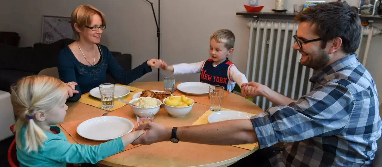 Familie h&auml;lt H&auml;ndchen vor dem Essen. Kurze kindergebete sind ein sch&ouml;ner Brauch.
