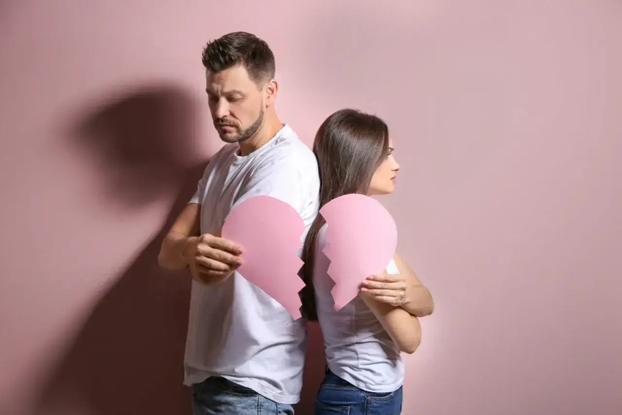 Pareja de espaldas, cada uno con la mitad de un corazón roto, reflejando un afecto intermitente y la distancia emocional.