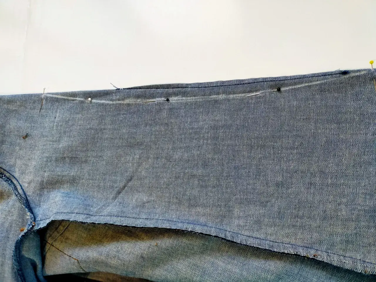 Szpilki wyznaczają linię cięcia, aby zwęzić koszulę damską. Widoczny denim i szew.