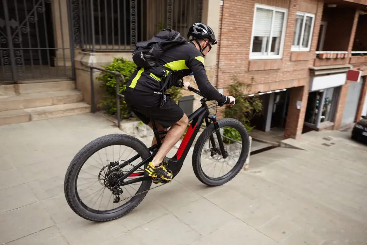 Man op een speed pedelec met helm en rugzak rijdt door een stadse straat. Het kenteken is niet zichtbaar.