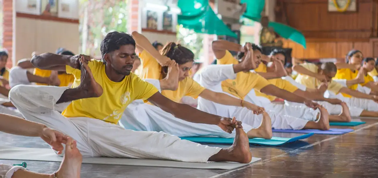 Grupo de personas practicando yoga Sivananda, estirando sus piernas y tocando sus pies.