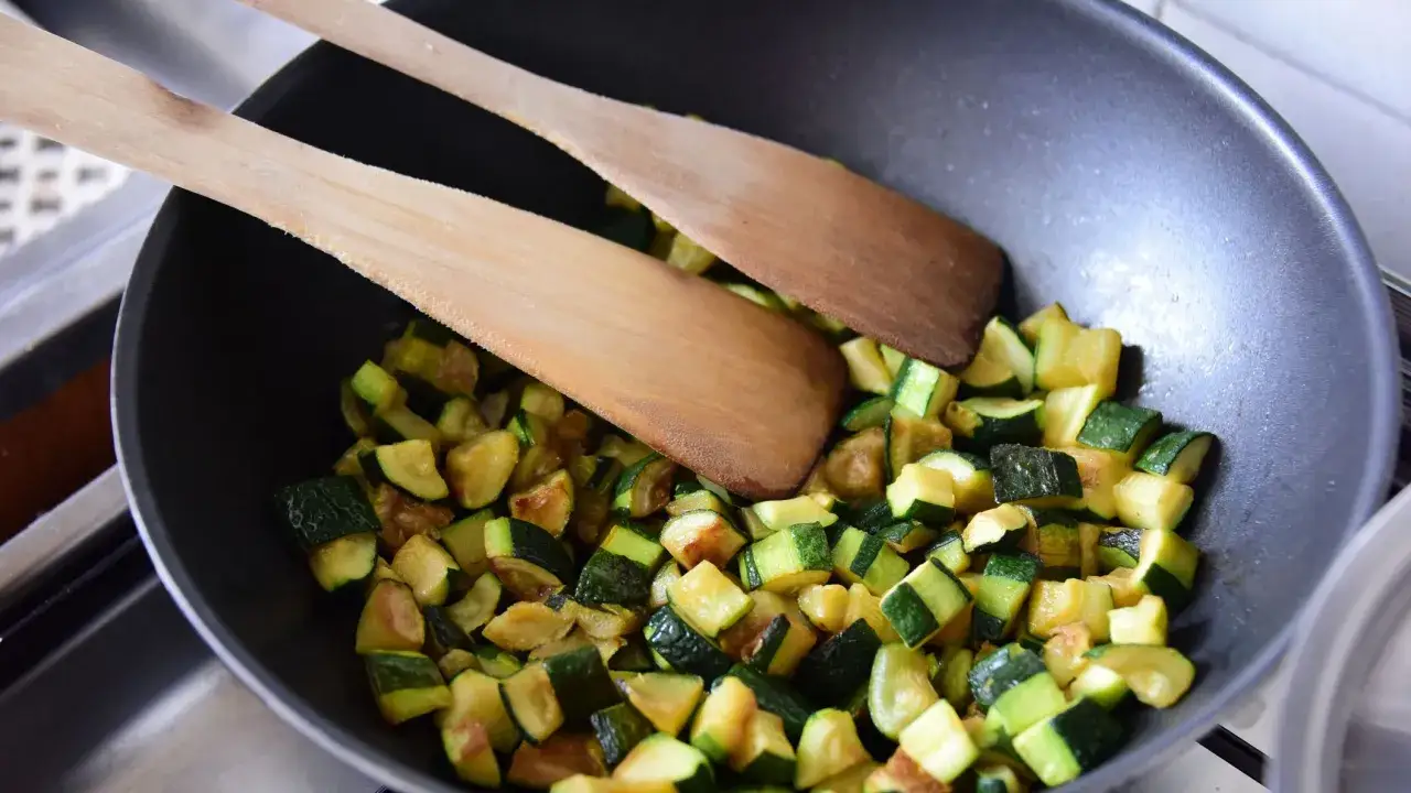 Zucchine tagliate a cubetti in padella, pronte per essere cucinate secondo le zucchine ricette della nonna. Due palette di legno le mescolano.