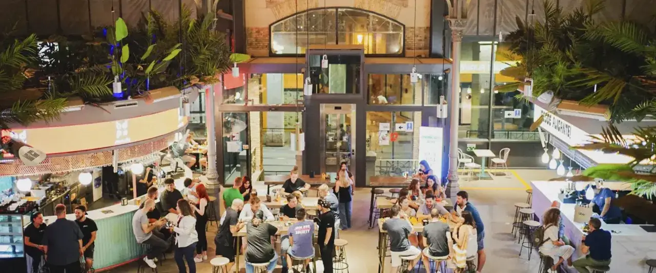 Gente disfrutando en el mercado central Zaragoza, con bares, mesas y mucha vegetación.