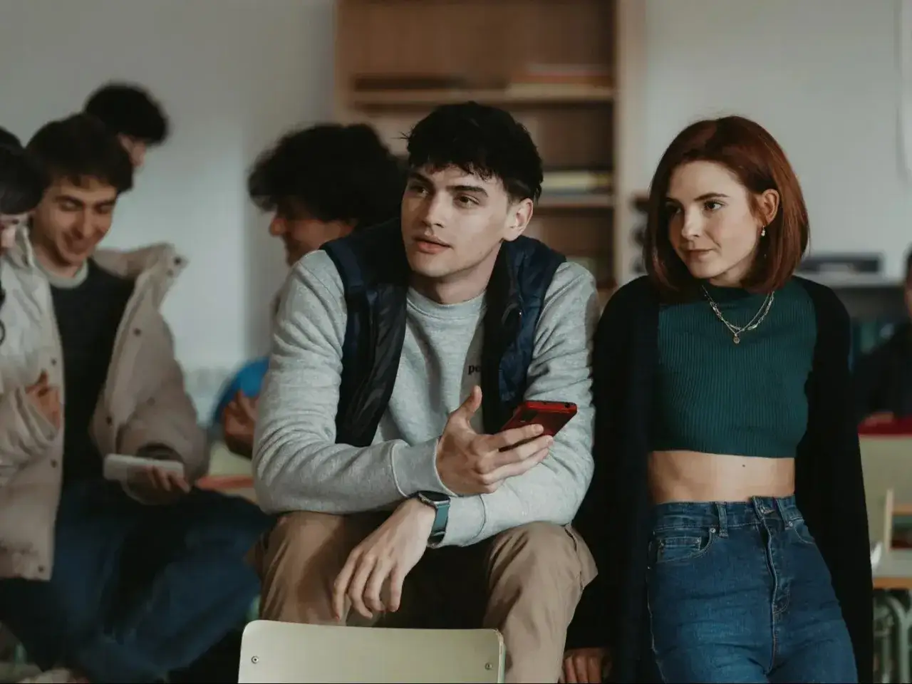 Nastolatkowie w szkole, jak z seriali Netflix dla nastolatków. Chłopak trzyma telefon, dziewczyna patrzy w bok.