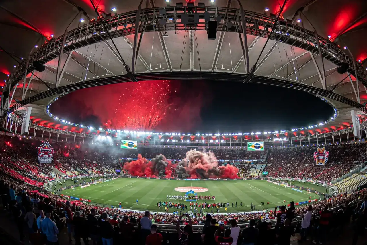 Estádio lotado com fogos e fumaça vermelha. Se você busca onde assistir Flamengo, este é o clima de um jogo inesquecível.