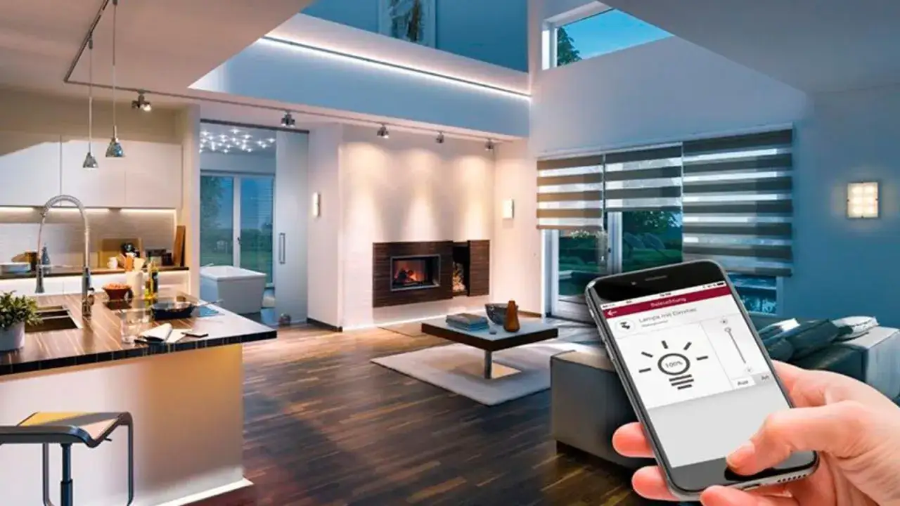 Mano sujetando smartphone con app de control de iluminaci&oacute;n dom&oacute;tica, ajustando la intensidad de las luces en un sal&oacute;n moderno con chimenea y cocina integrada.