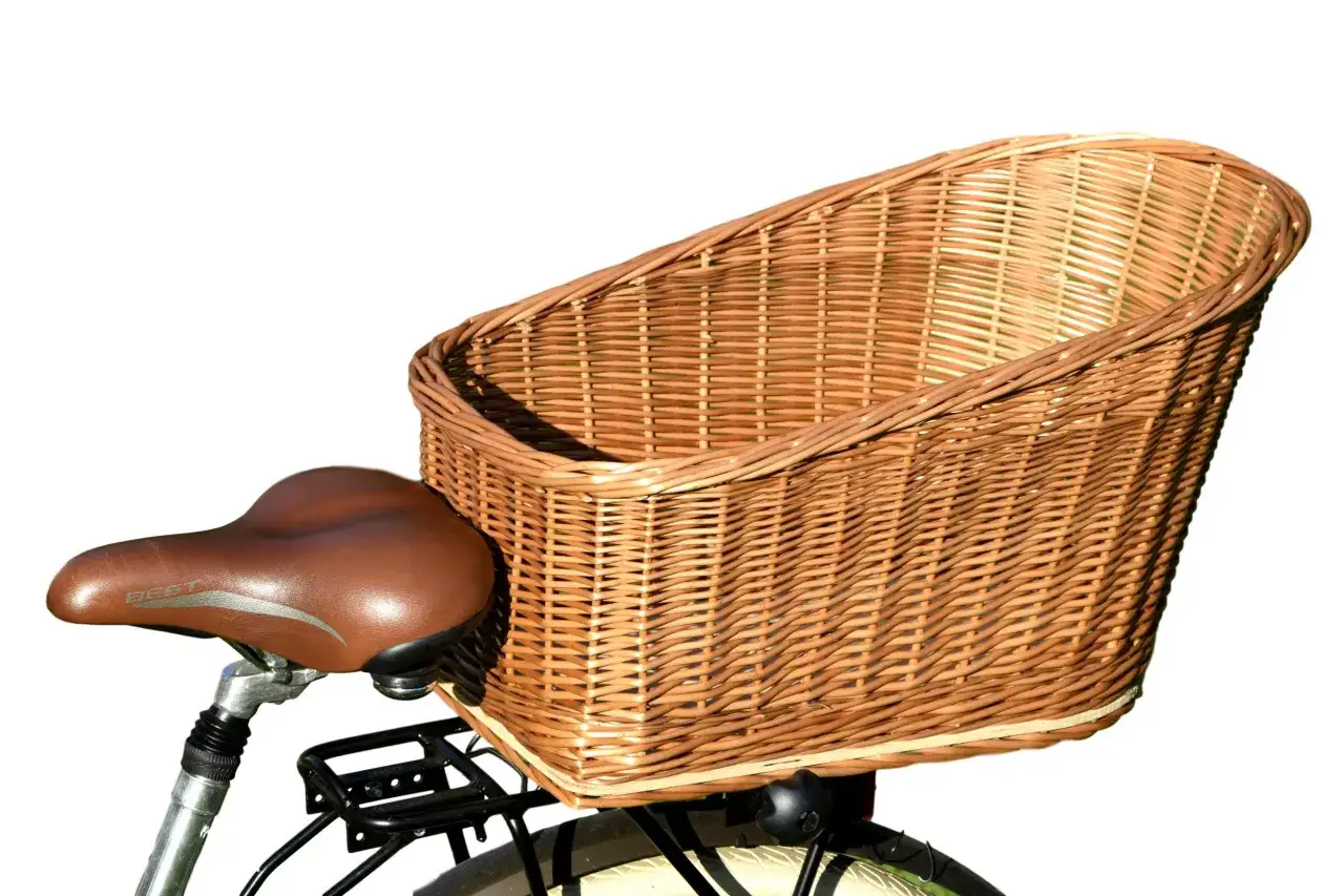 Pleciony koszyczek do rowerka, idealny na zakupy lub piknik. Brązowe siodełko rowerowe obok.