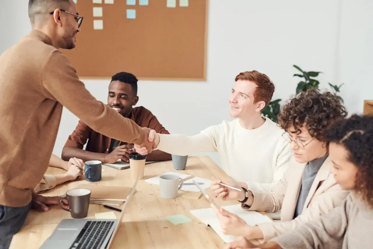 Equipo diverso en reuni&oacute;n, estrechando manos. Un buen ambiente para mejorar la comunicaci&oacute;n interna de una empresa.