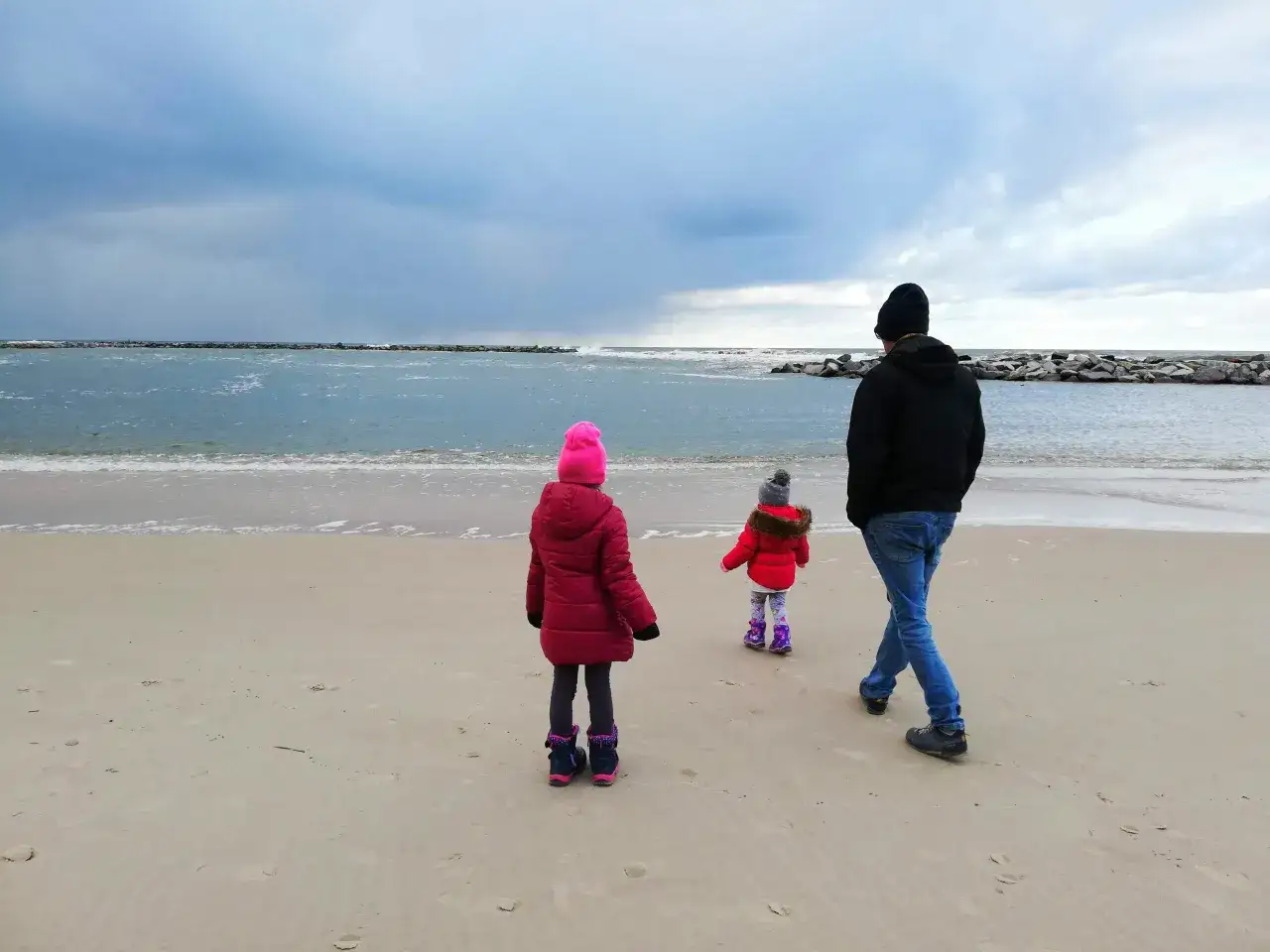Rodzina spaceruje po plaży zimą. Ojciec z dwójką dzieci, gdzie nad morze z dzieckiem zimą to świetny pomysł na aktywny wypoczynek.