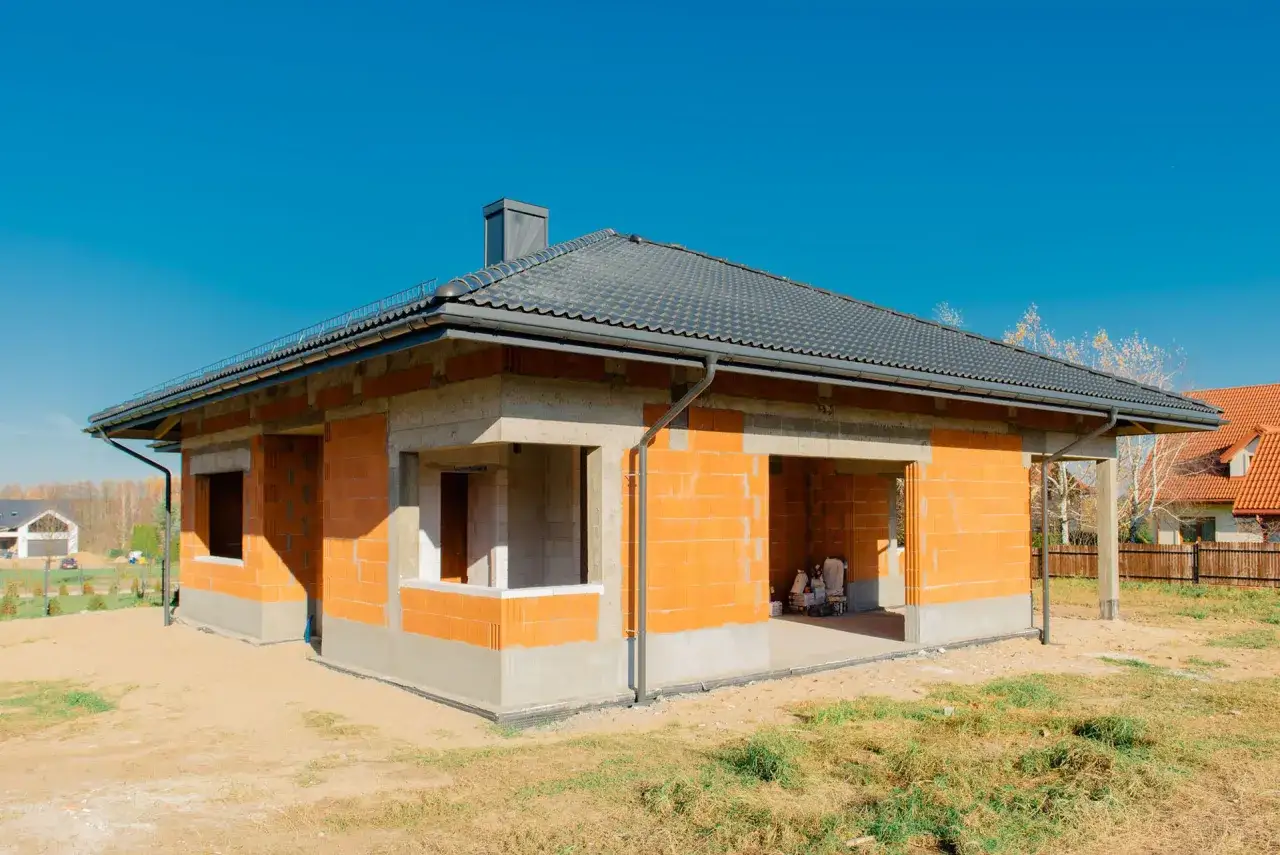 Budowa domu z pomarańczowej cegły pod niebieskim niebem.