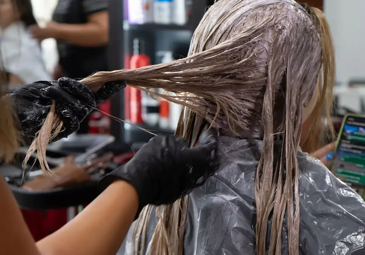 Friseur tr&auml;gt Handschuhe und tr&auml;gt Farbe auf das Haar auf. Die Frage, wie lange muss Farbe beim Friseur einwirken, ist entscheidend f&uuml;r das Ergebnis.
