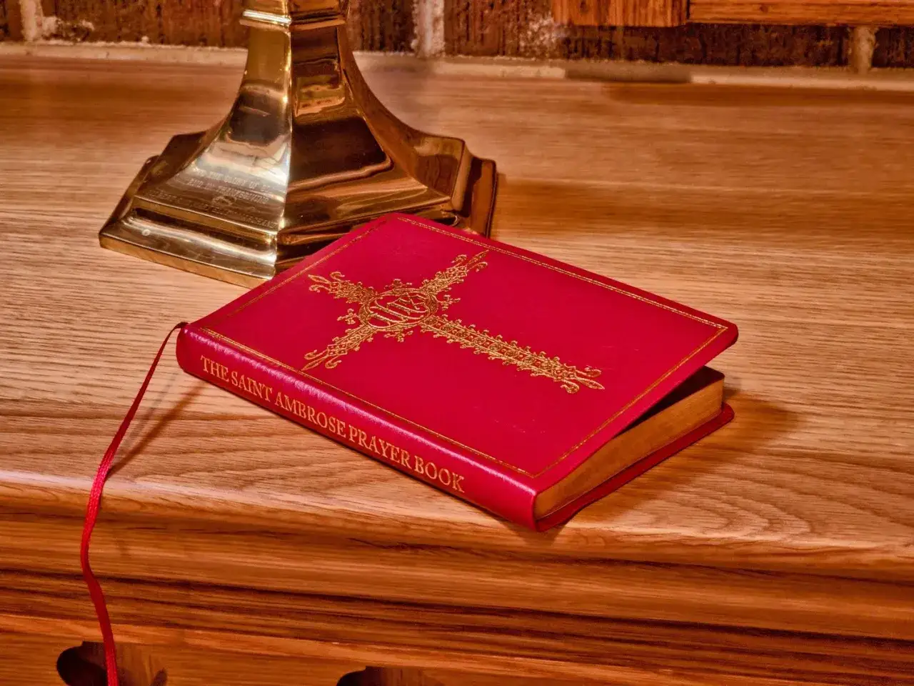 A red Saint Ambrose Prayer Book with a gold cross, ready for learning how to say prayers.