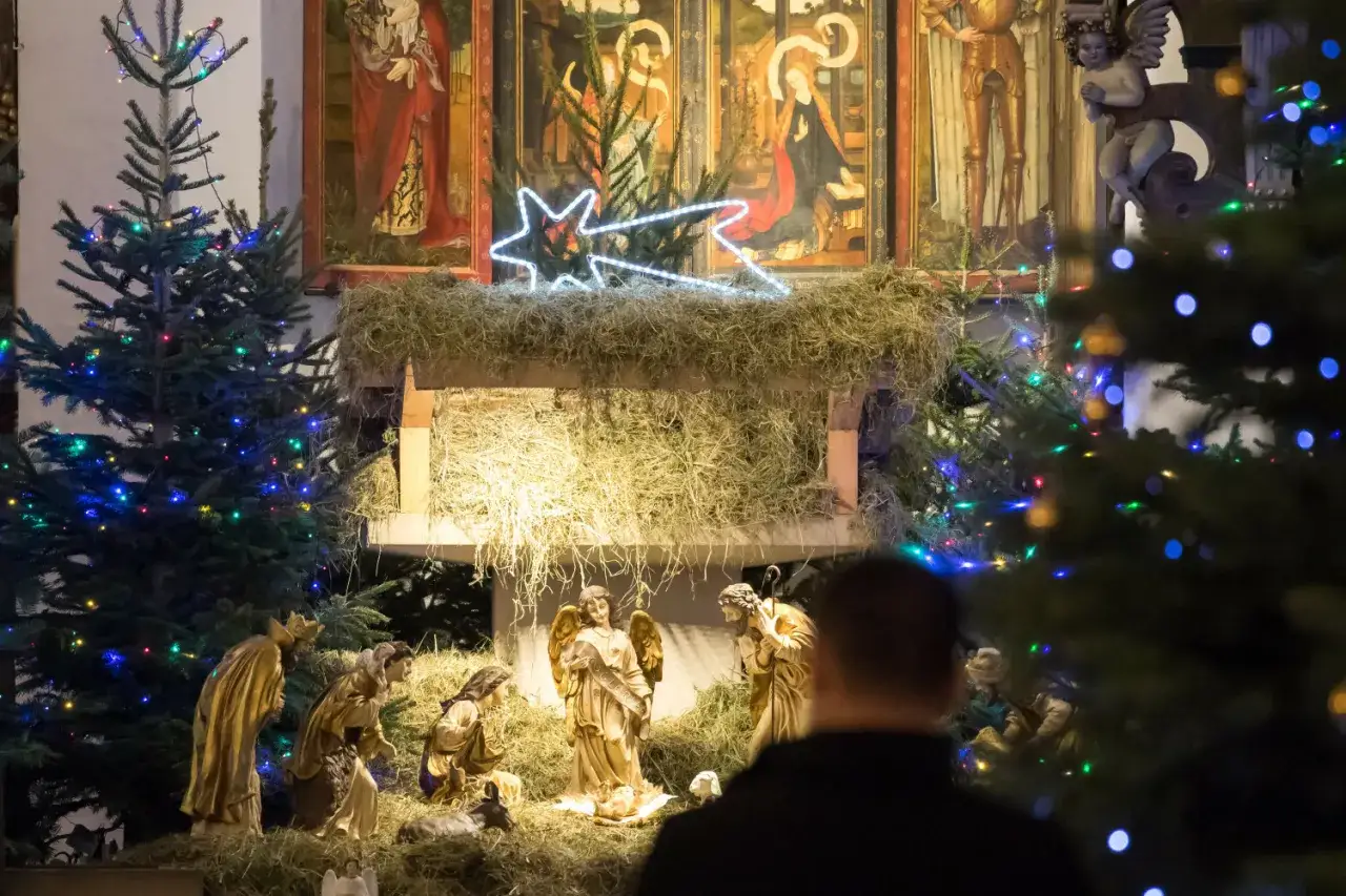 Bożonarodzeniowa pasterka w kościele. Figurki przedstawiają scenę narodzin Jezusa, otoczone choinkami i świątecznymi ozdobami.