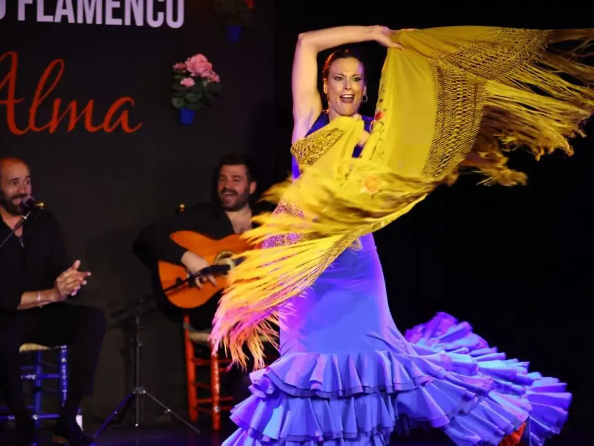Una bailaora de flamenco, con un vestido azul y un mantón amarillo, se mueve al ritmo de la guitarra en unas rumbas flamencas.