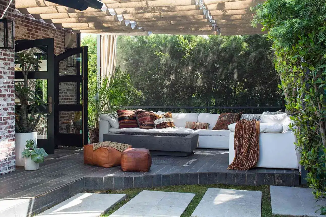 Aménagement coin détente extérieur avec canapé blanc, coussins ethniques, poufs en cuir et foyer central. Parfait pour se relaxer.