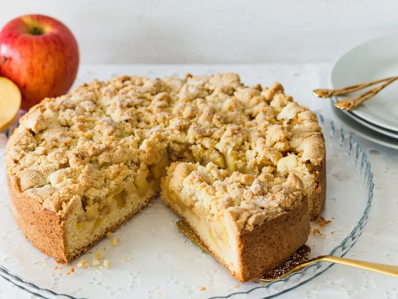 Ein saftiger Apfel-Streuselkuchen, perfekt für den sonntagskuchen schnell und einfach. Daneben liegen rote Äpfel.