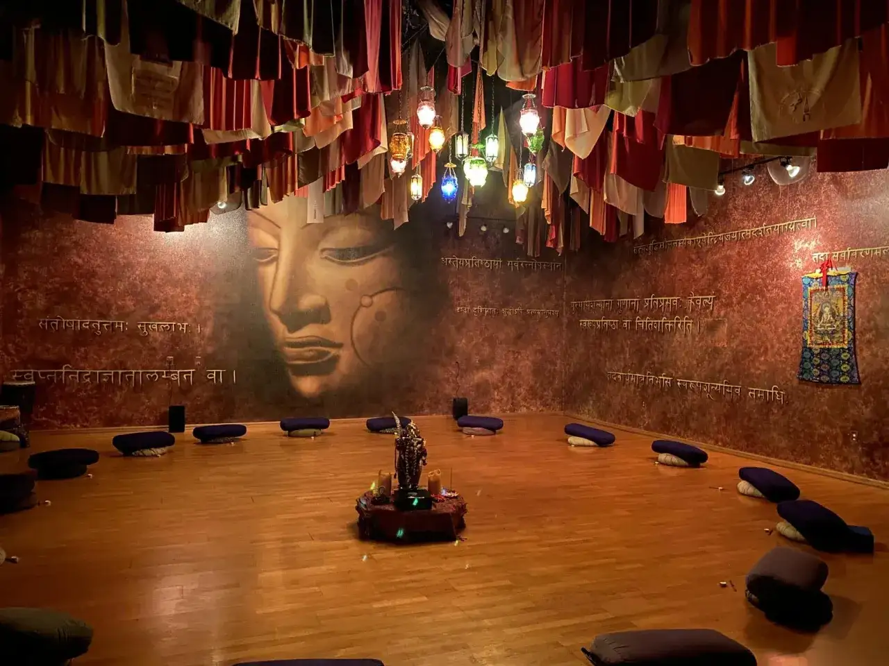 Sala de meditación con cojines, un mural de Buda y luces colgantes. El ambiente evoca el samadhi, significado de unión y paz interior.