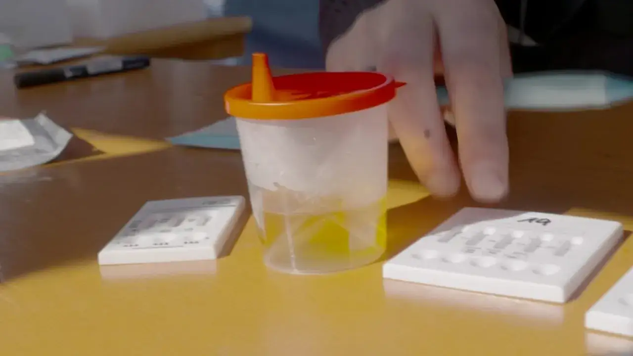 Teststreifen und ein Becher mit Urin f&uuml;r einen thc bluttest liegen auf einem Tisch.