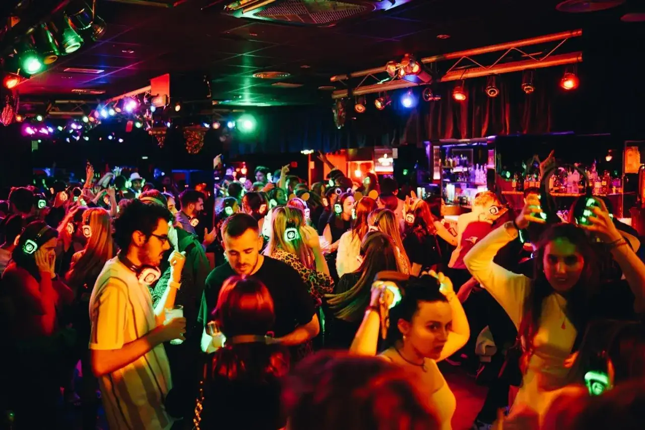 A lively crowd dances at a silent disco, a popular spot among gay bars in Valencia. People wear glowing headphones, enjoying the music and vibrant atmosphere.