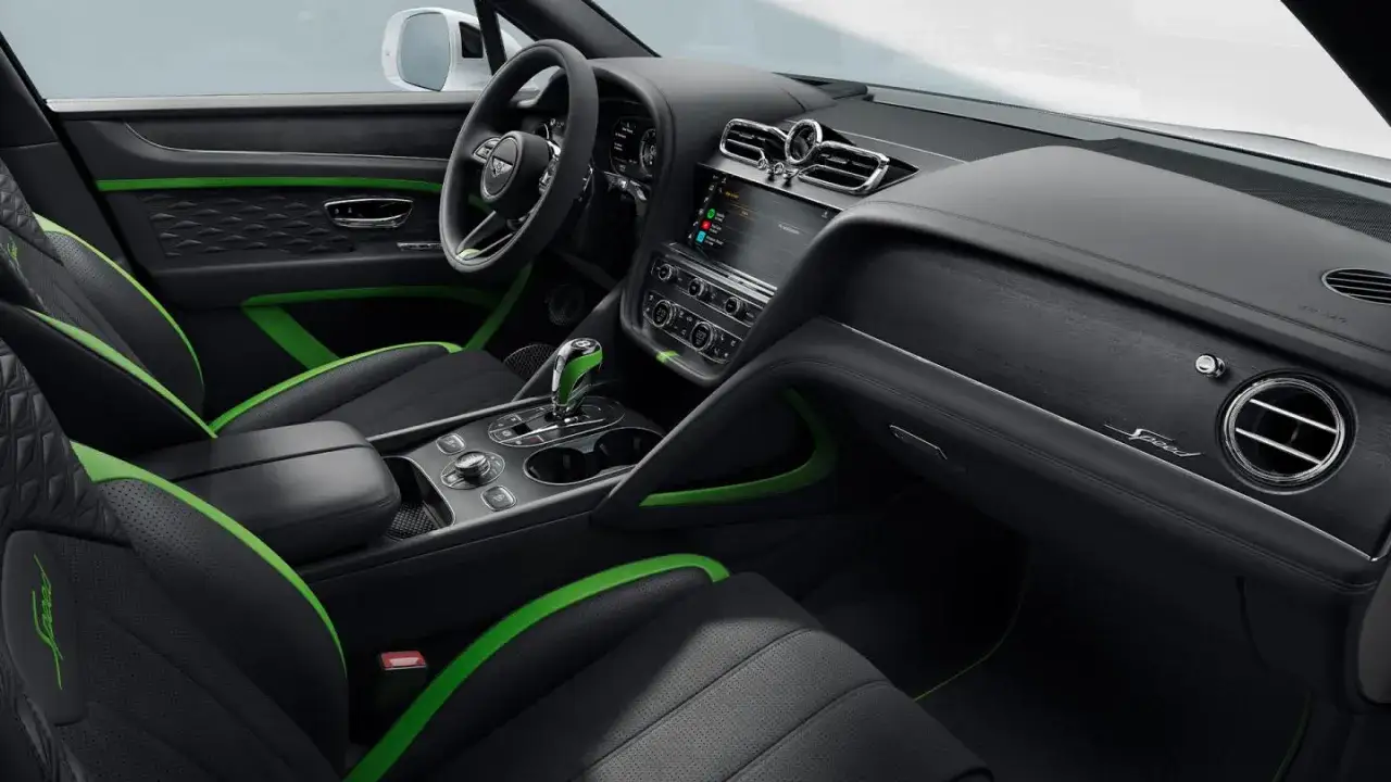 Wnętrze Bentley SUV z czarną tapicerką i zielonymi akcentami. Widoczny ekran multimediów, kierownica i dźwignia zmiany biegów.