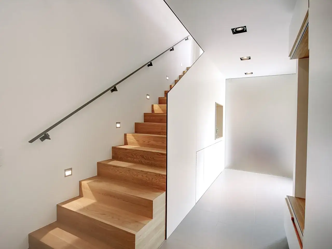 Moderne Treppen aus Holz in einem Einfamilienhaus, beleuchtet von kleinen Wandleuchten und Deckenstrahlern.