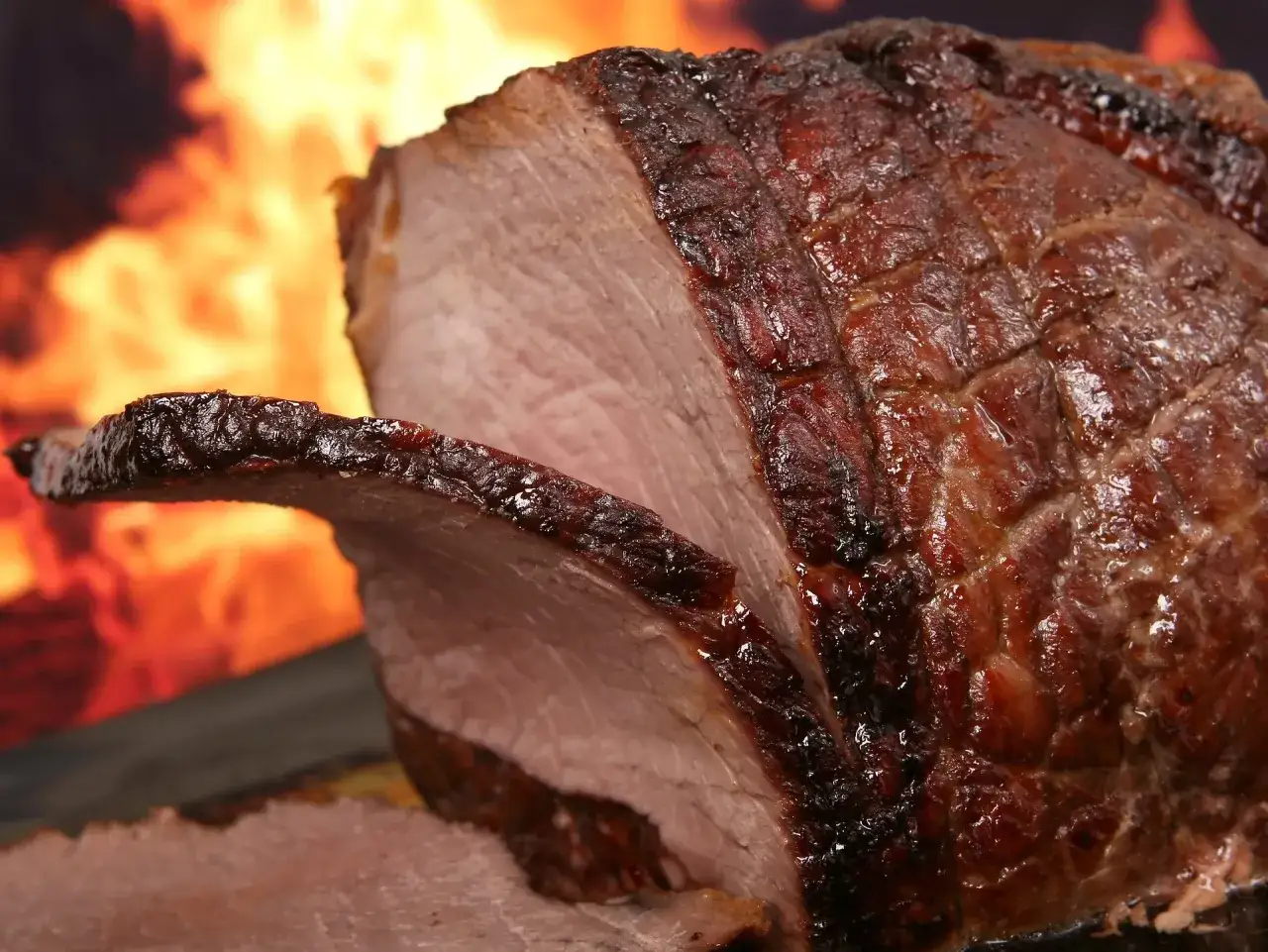 Un enchaud de porc juteux, rôti à la perfection, avec une croûte caramélisée et une chair rosée, devant un feu de bois ardent.