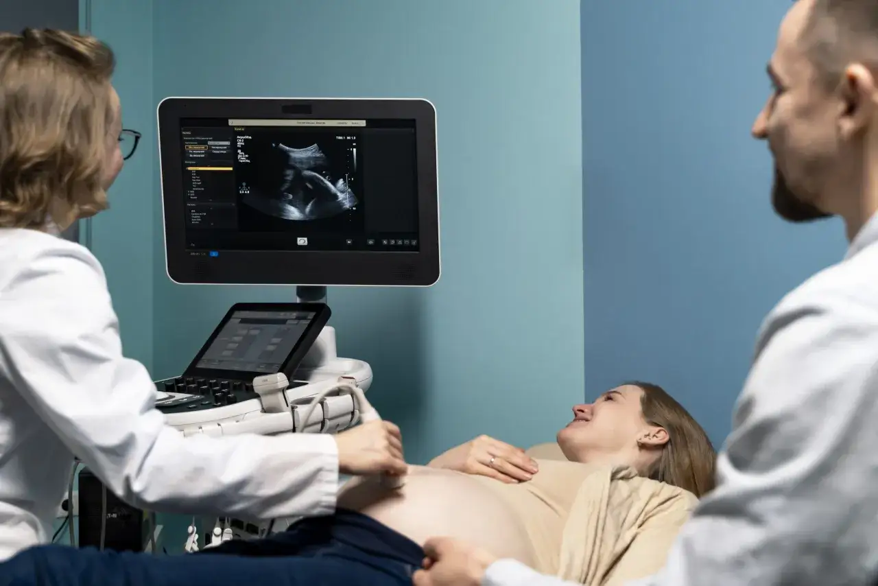 Jak przygotować się do pierwszego badania prenatalnego? Lekarz wykonuje USG ciężarnej, na ekranie widać obraz płodu.