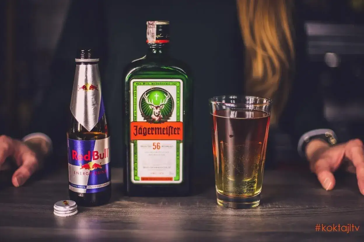 Na blacie stoją butelka Jägermeistera, puszka Red Bulla i szklanka z drinkiem.