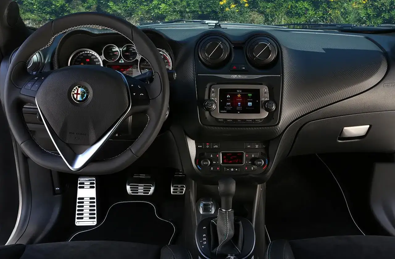 Wnętrze małego szybkiego auta Alfa Romeo. Kierownica, deska rozdzielcza z ekranem multimedialnym i sportowe pedały.