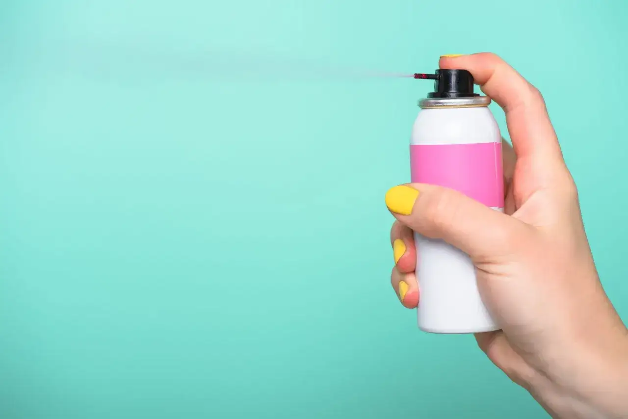 Hand spr&uuml;ht mit Spraydose, um Lippenstiftflecken zu entfernen.