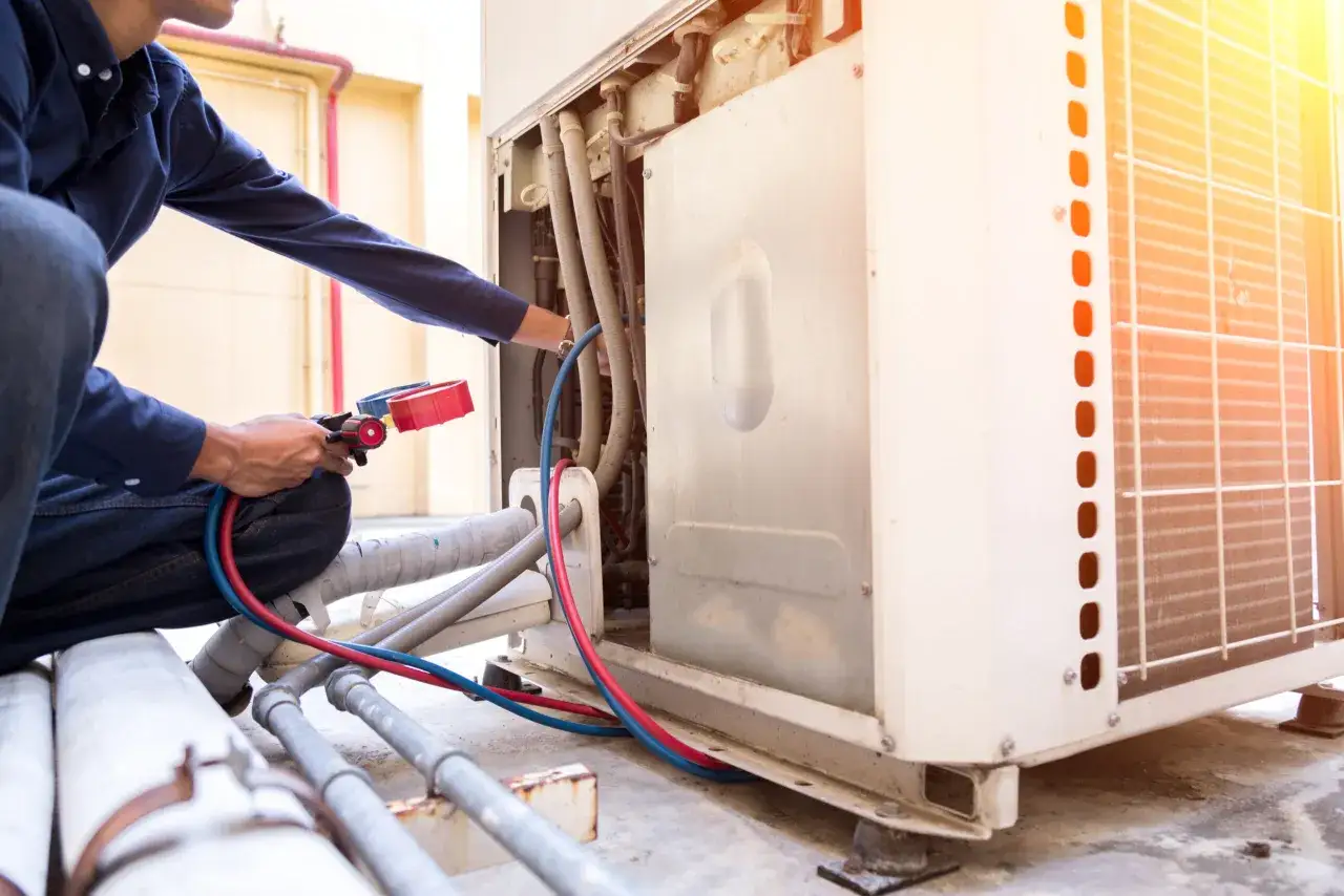 Técnico realiza soldadura con nitrógeno en unidad de aire acondicionado exterior, conectando manómetros y mangueras.