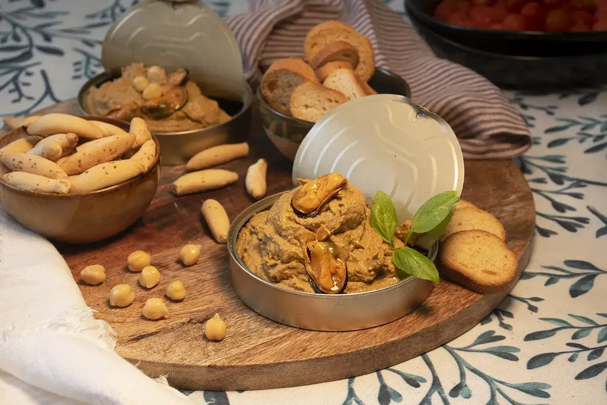 Delicioso paté de mejillones en escabeche, servido con grissini, tostadas y garbanzos. ¡Un aperitivo perfecto!