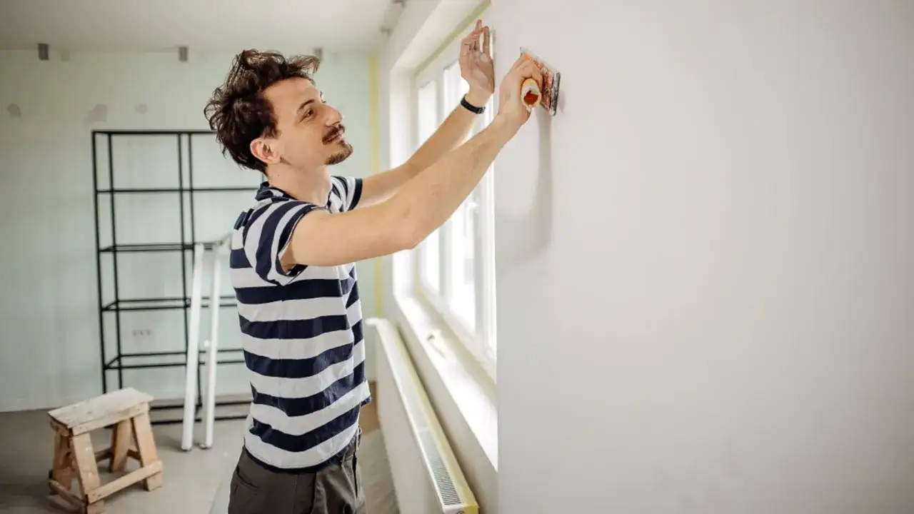 Hombre aplicando masilla para reparar el gotele rayado de la pared.
